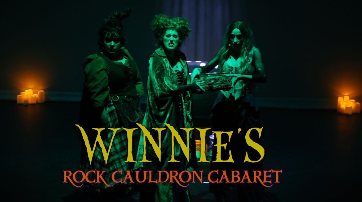 Three people in witch costumes stand on a dark stage with glowing candles in the background. The text "Winnie's Rock Cauldron Cabaret" appears in yellow and red letters at the bottom of the image.