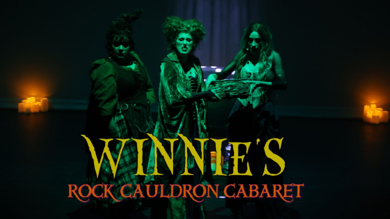 Three people in witch costumes stand on a dark stage with glowing candles in the background. The text "Winnie's Rock Cauldron Cabaret" appears in yellow and red letters at the bottom of the image.