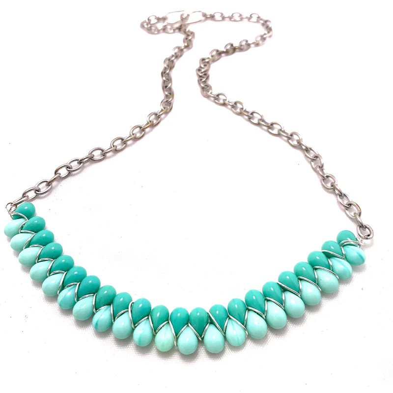 A silver chain necklace with turquoise teardrop-shaped beads arranged in a row, each bead wrapped with thin silver wire—a stunning example of twisted bead jewelry, beautifully displayed on a white background.