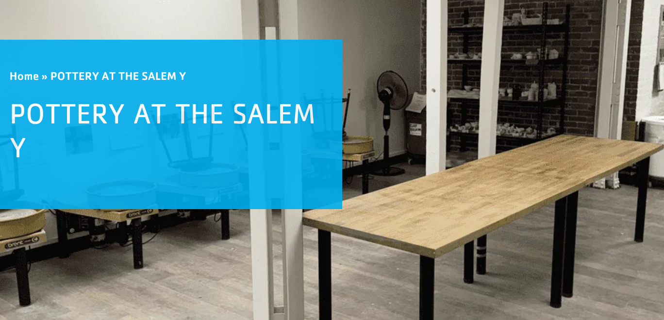 A pottery studio with pottery wheels against the back wall, shelves holding supplies, a large wooden table in the center, and a standing fan in the corner. A blue overlay reads "You and Me Claymakers: POTTERY AT THE SALEM Y.