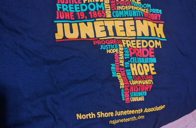 A blue shirt featuring a colorful "JUNETEENTH" design, surrounded by words like freedom, pride, hope, and history. Includes North Shore Juneteenth Association text and nsjuneteenth.com—perfect for Revere's Flag Raising Ceremony.