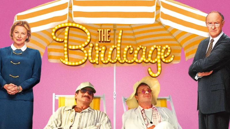 Four people pose in front of a pink background with a yellow-and-white striped umbrella displaying "The Birdcage." Two relax in lounge chairs wearing light clothing, while two stand behind them dressed in business attire, evoking The Birdcage vibe.