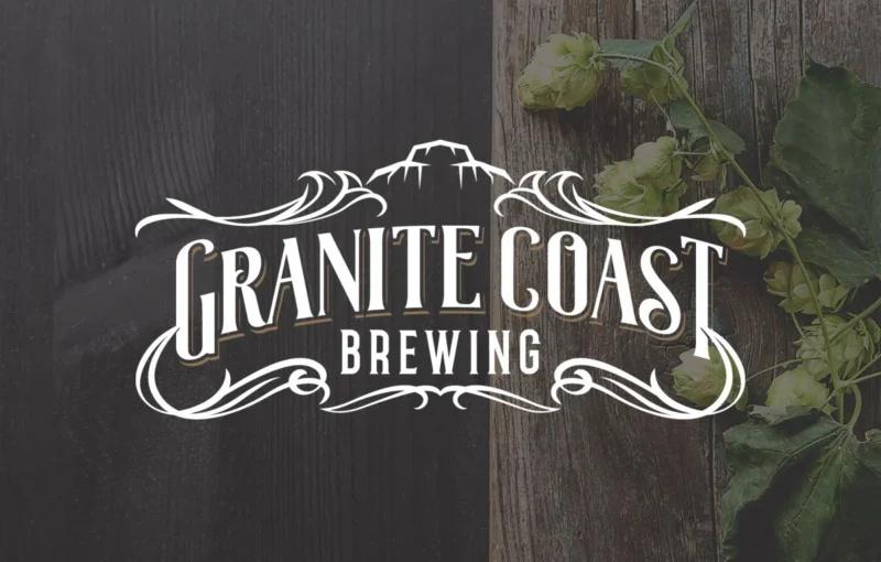 A white Granite Coast Brewing logo with mountain and decorative flourishes is centered over a background of dark and light wooden planks with green hops on the right side.