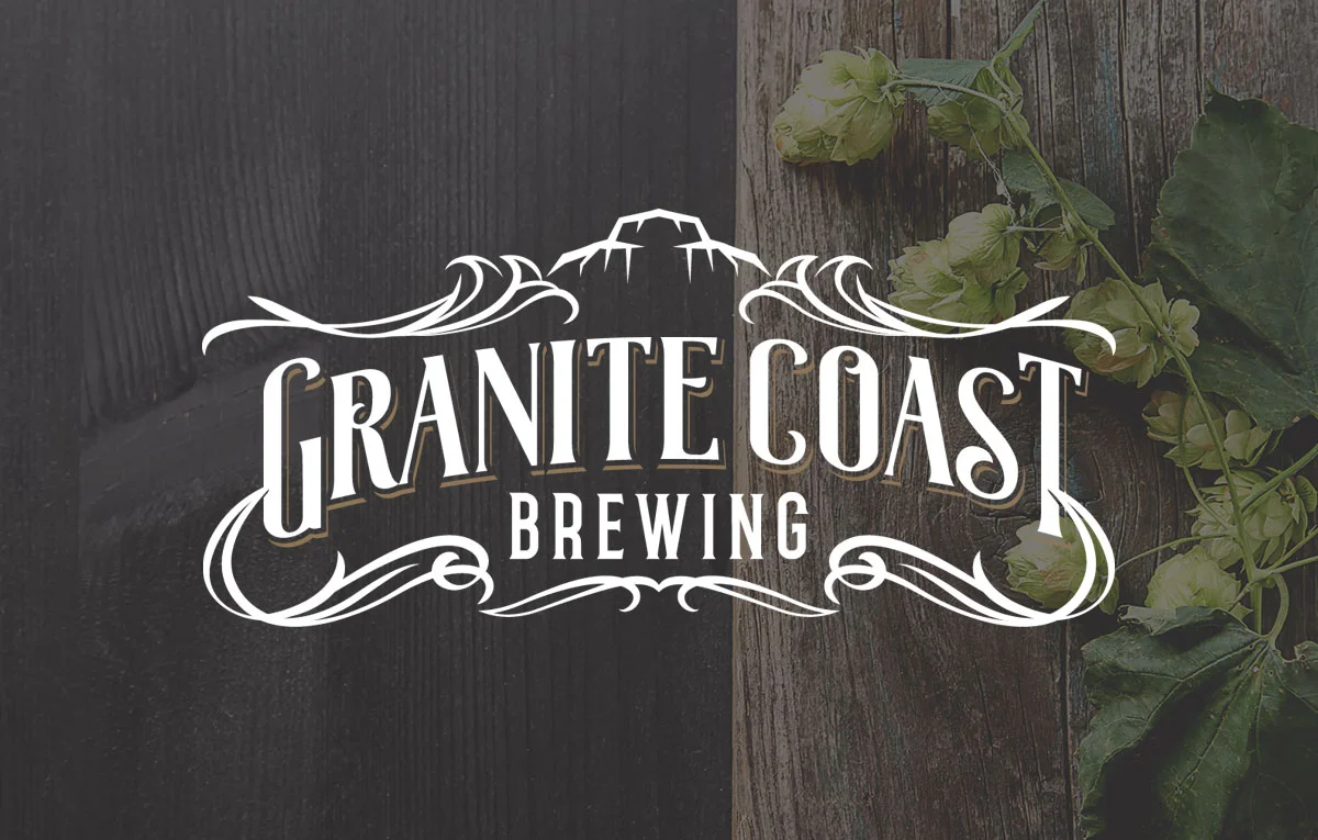 A white Granite Coast Brewing logo with mountain and decorative flourishes is centered over a background of dark and light wooden planks with green hops on the right side.