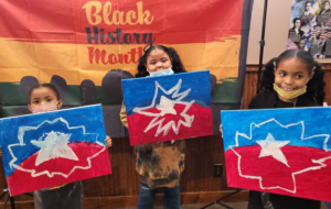 Three children from Essex County stand in front of a "Black History Month" banner, each holding an abstract red, blue, and white painting. Two have masks under their chins and all are smiling, celebrating creativity at the CCE Nightlife event.