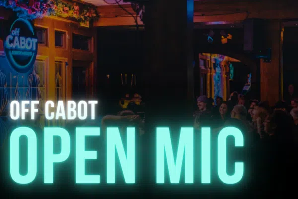 A dimly lit venue with people seated at tables; a sign on the wall reads "OFF CABOT." Large text in the foreground says "Comedy Open Mic.