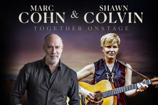 Marc Cohn and Shawn Colvin stand side by side in front of a twilight sky background. Marc wears a dark shirt and vest, while Shawn holds an acoustic guitar and wears a sleeveless top. Text above reads: “Marc Cohn & Shawn Colvin Together Onstage.”.