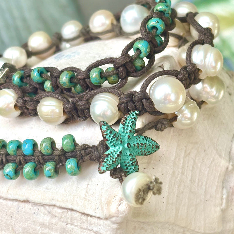 A close-up of a handmade bracelet featuring white pearls, turquoise beads, brown cord, and a turquoise starfish-shaped charm, arranged on a light textured surface.