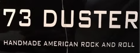 Black background with bold white text reading "73 DUSTER" and smaller text below stating "HANDMADE AMERICAN ROCK AND ROLL.