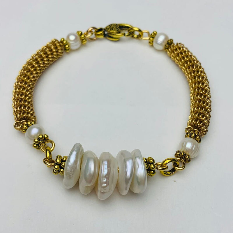 A bracelet featuring five irregular white pearls at the center, gold metal chain links, small round white pearls on either side, and an ornate gold clasp, all arranged in a circle on a plain white background.