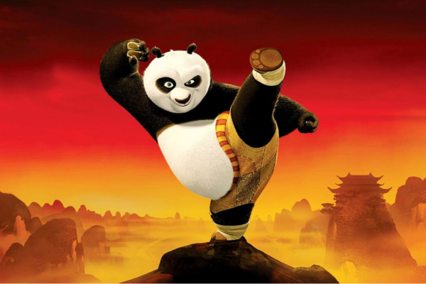 An animated panda in martial arts attire strikes a high kick pose atop a rock, with a misty, mountainous landscape and a distant traditional building in the orange-red background.