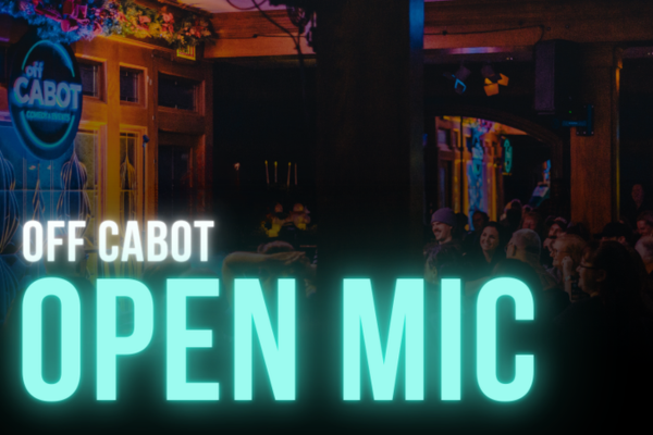 A sign reading "OFF CABOT OPEN MIC" glows in teal in a dimly lit venue, with people sitting and standing in the audience. Warm lighting and indoor plants decorate the space.