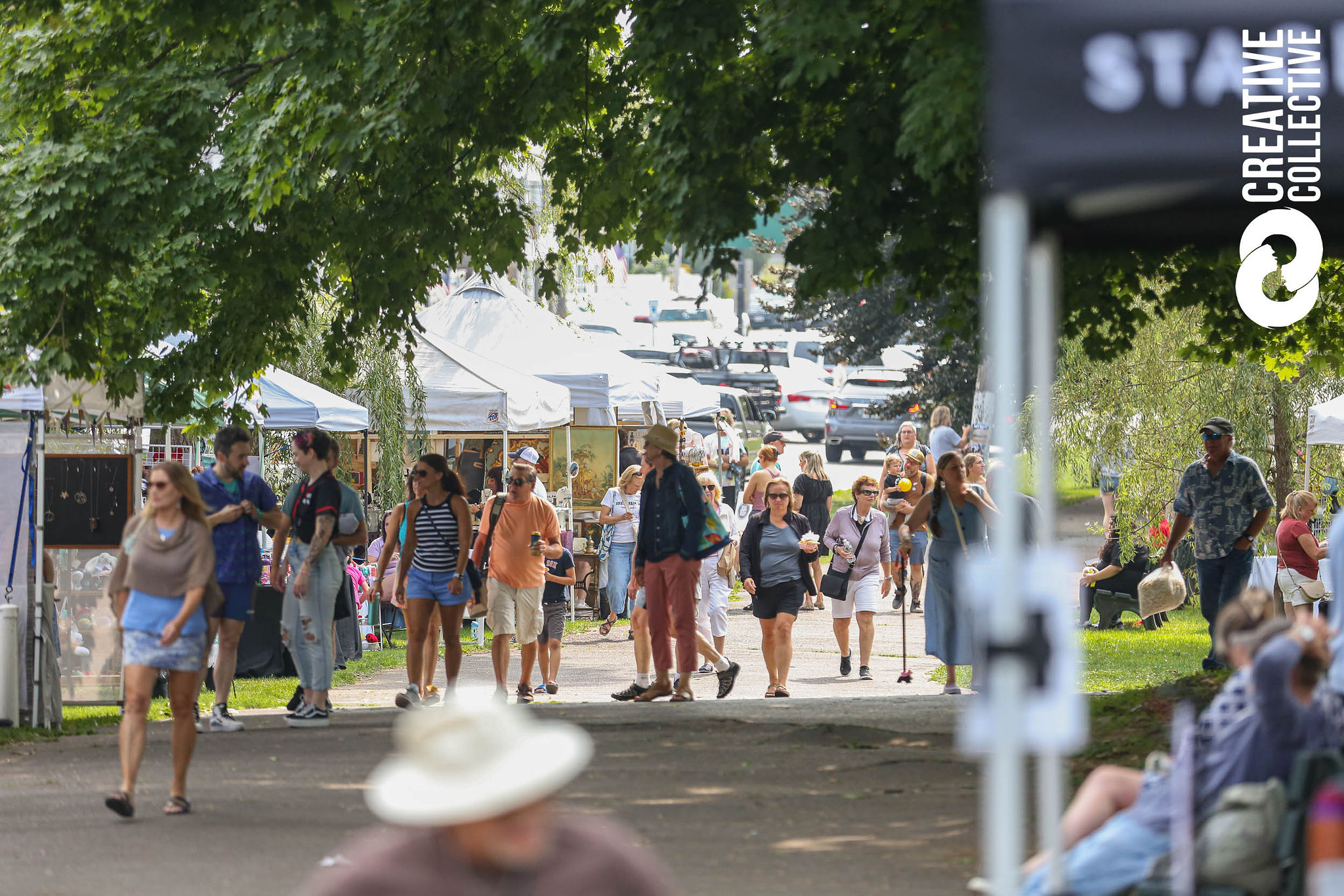 People stroll a tree-lined path at an outdoor event, shopping at white vendor tents. Some wear hats or carry bags. Cars are parked behind, and the "Creative Collective" logo appears right, hinting at the Salem Jazz and Soul Festival 2026 atmosphere.