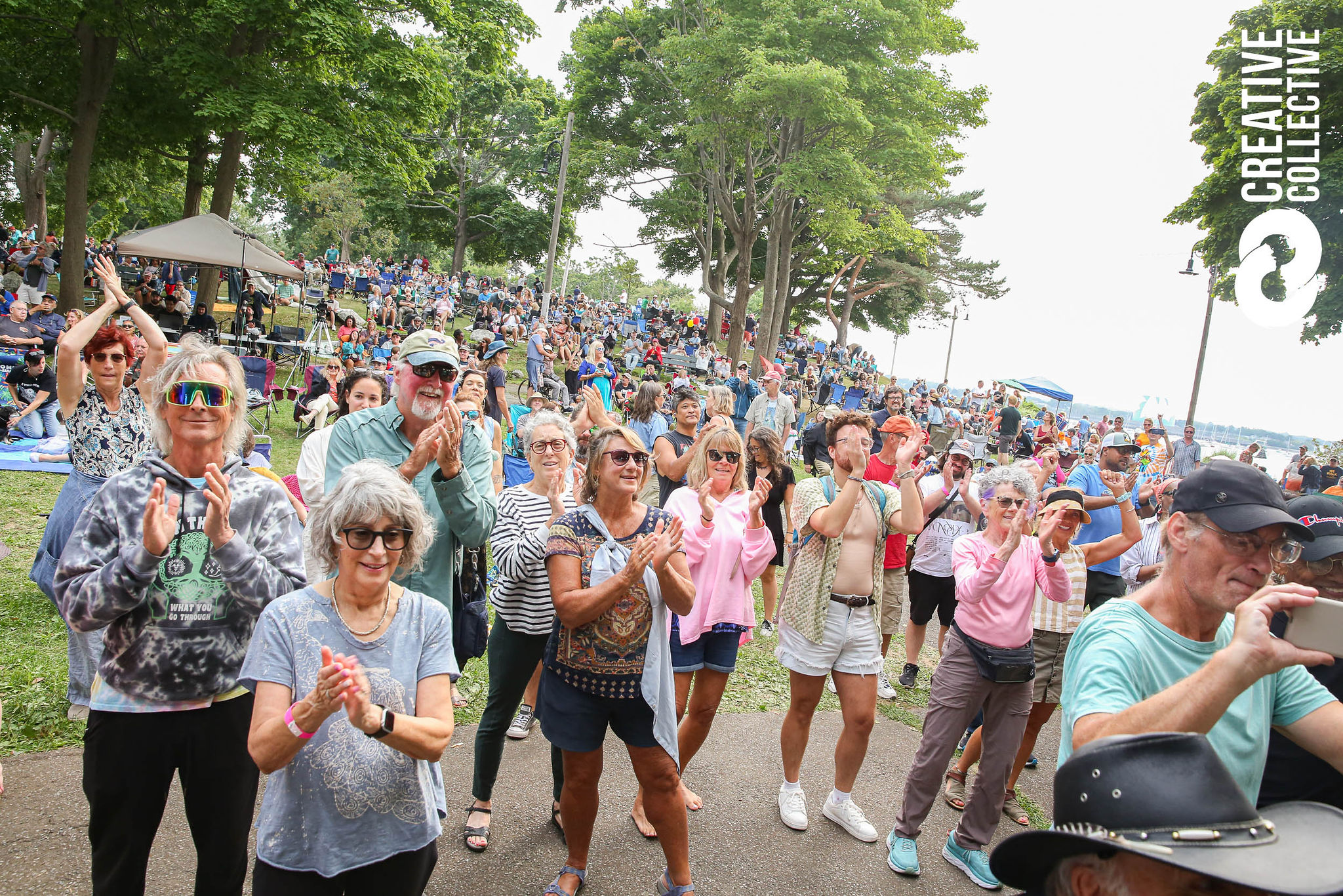 A large crowd of people, mostly older adults, stands outdoors in a park clapping and enjoying the Salem Jazz and Soul Festival 2026. Trees and lawn surround the gathering, with more seated on the grass. "CREATIVE COLLECTIVE" text is visible on the right.