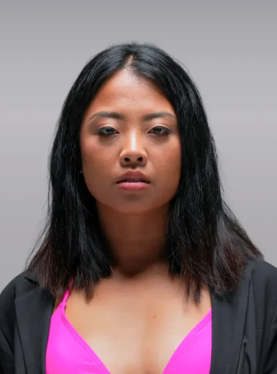 A person with straight, shoulder-length black hair is facing forward. They are wearing a black jacket over a bright pink top, with a neutral expression against a plain gray background that evokes a contemporary and modern design aesthetic.