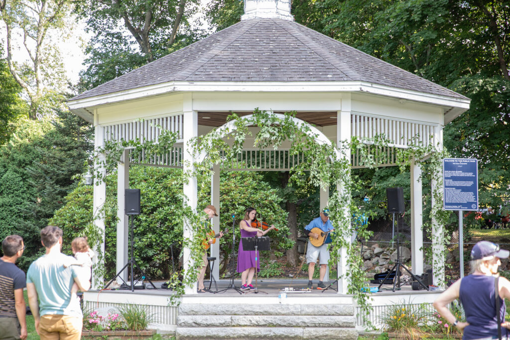 Musicians perform in the vine-draped white gazebo on Beverly Common as a small crowd listens on the grass at the Beverly Garden Party