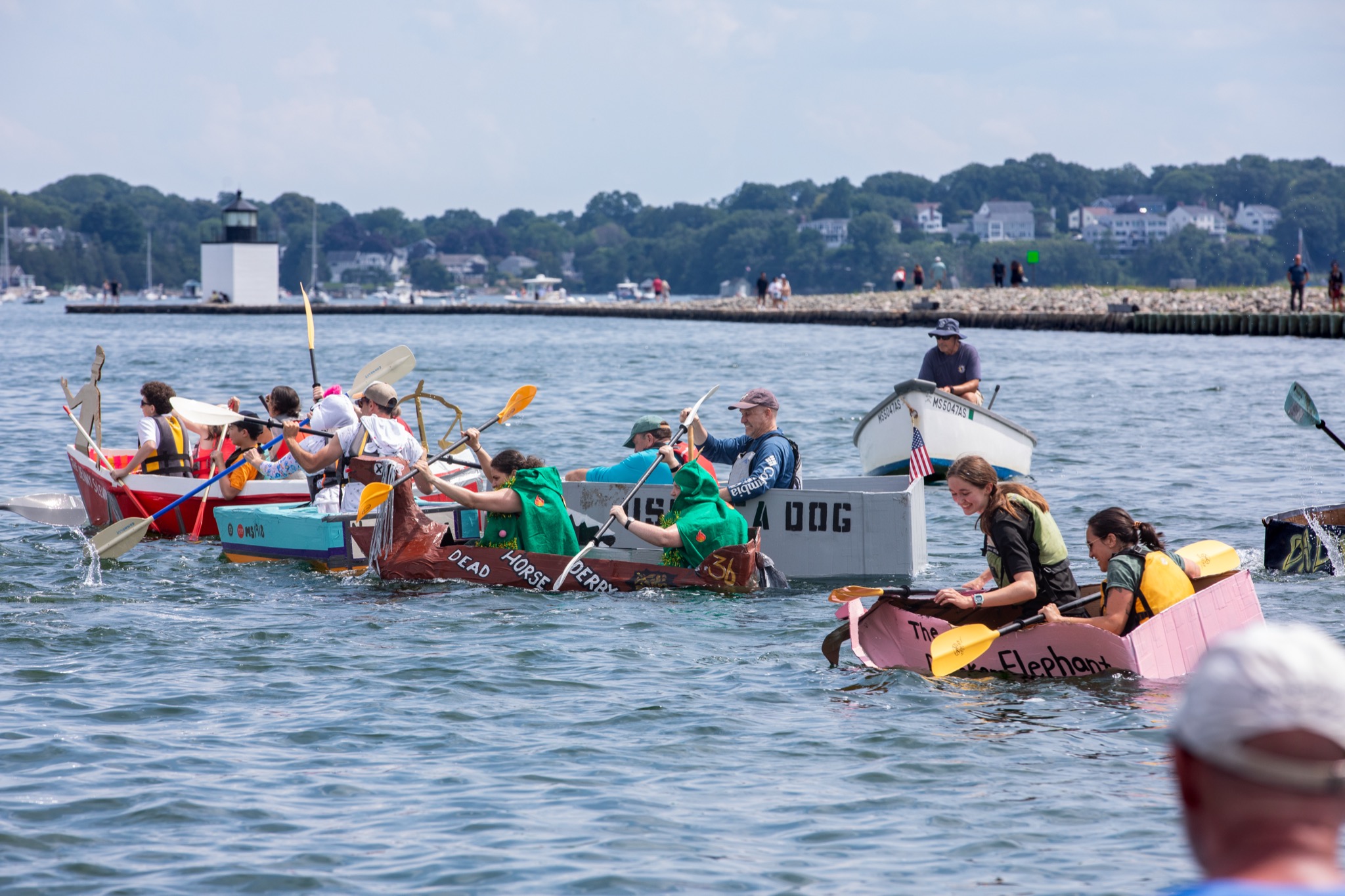 Fleet of cardboard boats racing with a lighthouse in the background in Salem Massachusetts