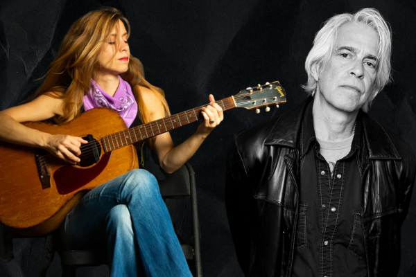 A woman sits playing an acoustic guitar, wearing a purple bandana and blue jeans. Beside her, a man with white hair in a black leather jacket stands against a dark background.