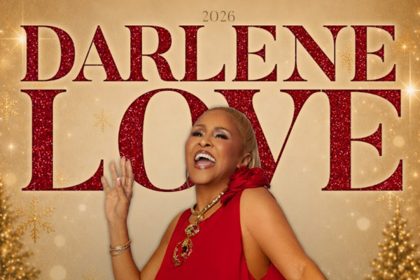 A woman in a red dress smiles and poses in front of large, glittery red text that reads “2026 DARLENE LOVE,” with gold snowflakes and two decorated Christmas trees visible at the edges of the image.