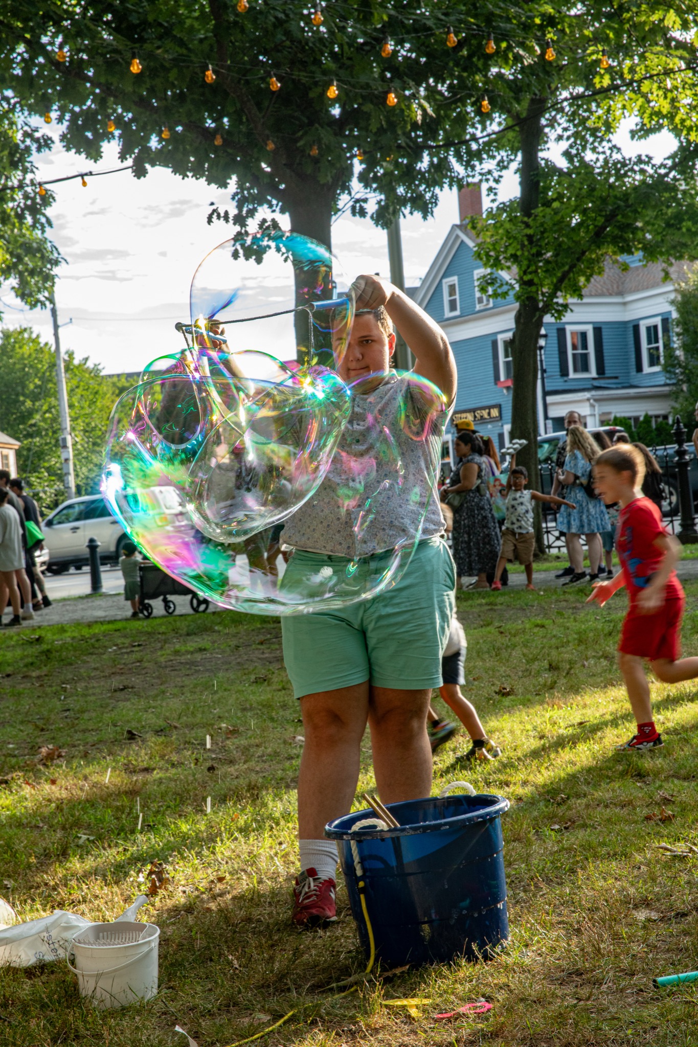 Kids chasing giant iridescent bubbles across the lawn at the Ice Scream Bowl on Salem Common