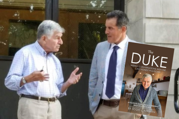 Two men stand outside a building having a conversation. One gestures with his hands. A book cover titled “The Duke” partially obscures the image, showing a man indoors and text about weekly political conversations.