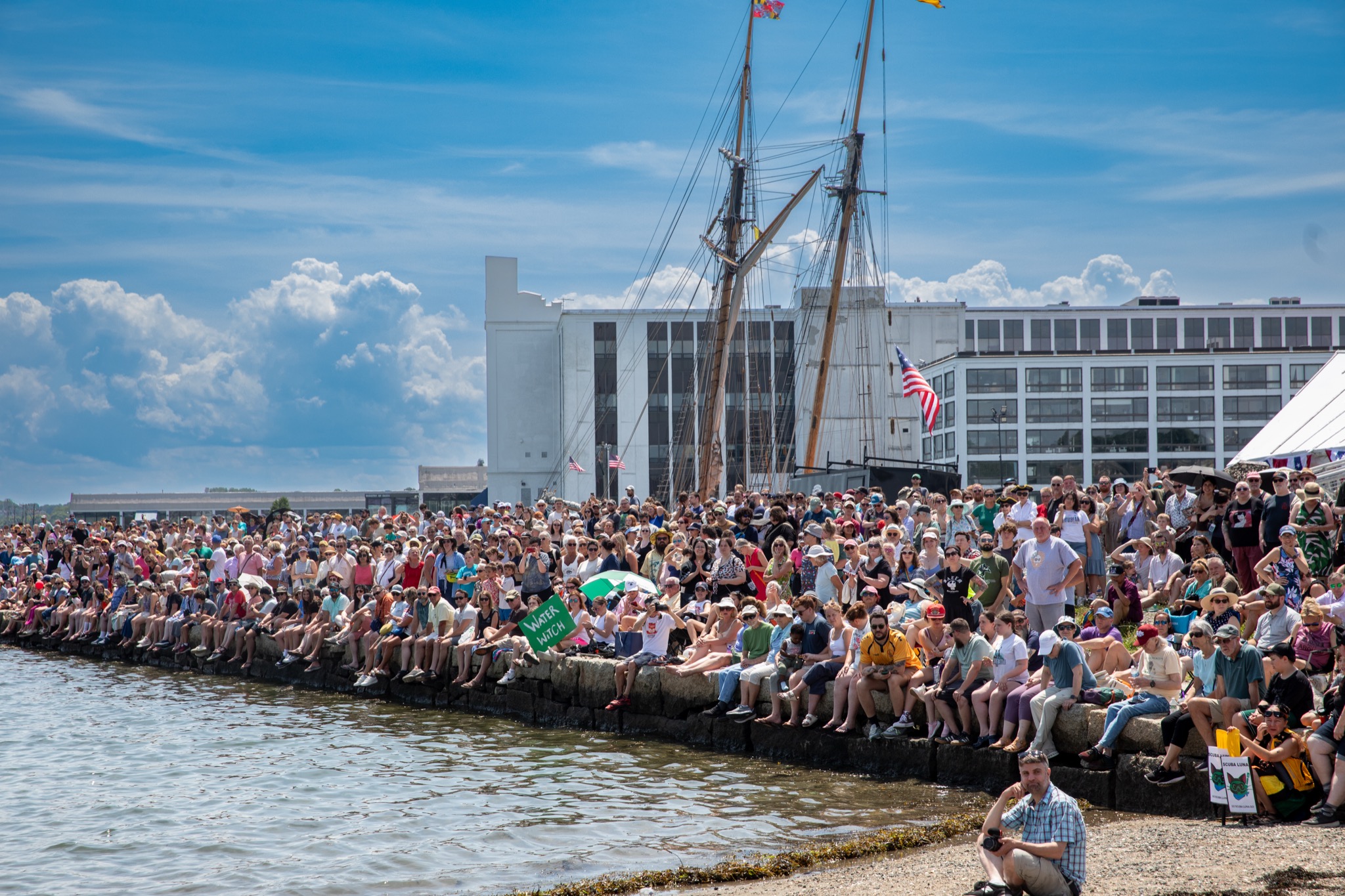 Spectators lining the Salem Harbor seawall with a tall ship in the background at the Salem 400 Maritime Festival