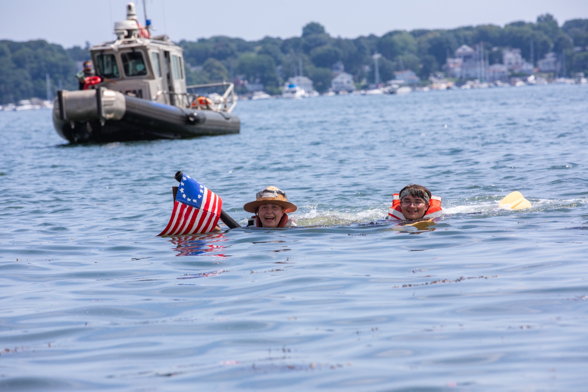 Swimmers holding a Betsy Ross flag beside their sunken cardboard boat in Salem Harbor