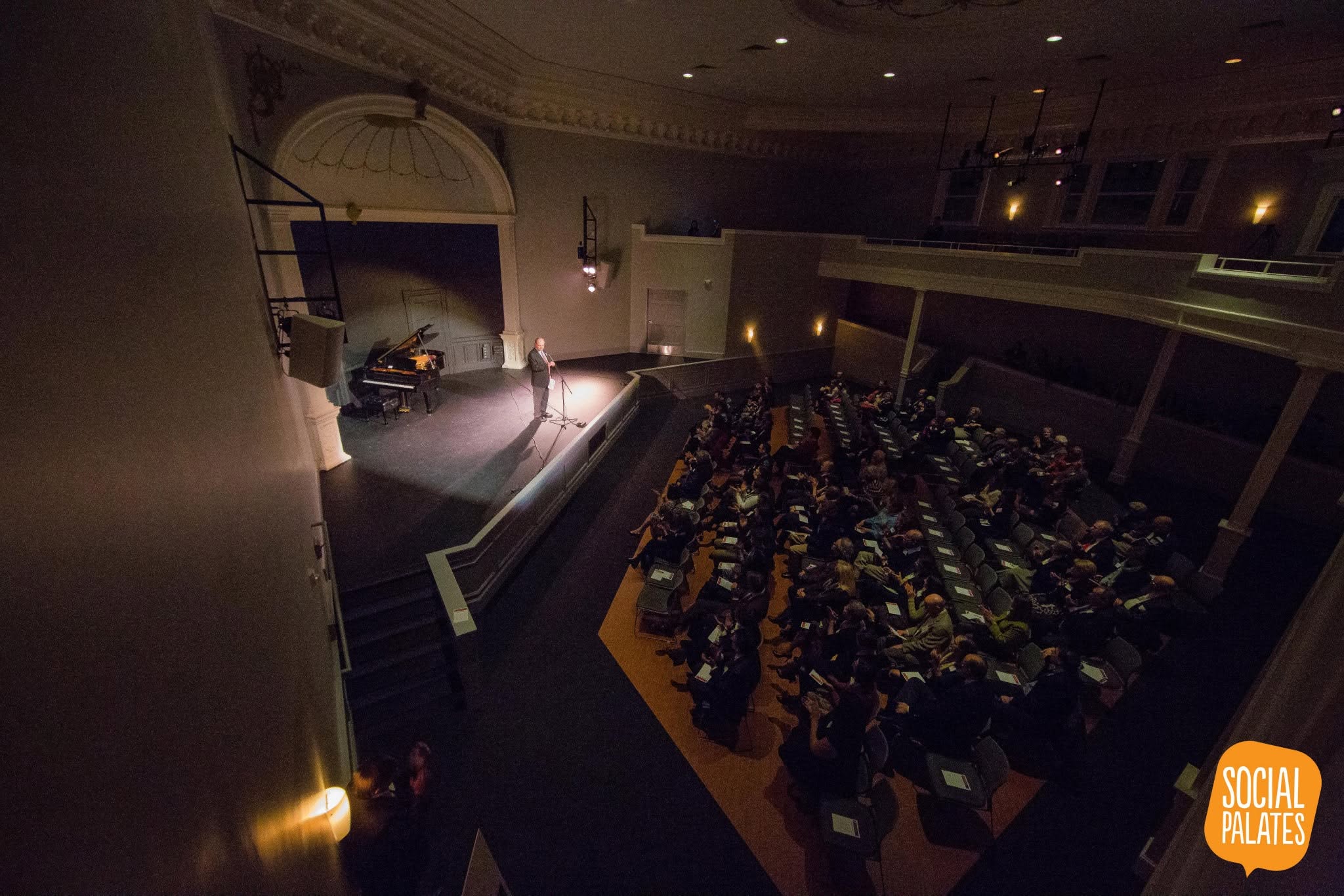 The restored auditorium of Ames Memorial Hall in Salem during a performance, seen from the balcony, with a grand piano on the lit stage and a full audience below