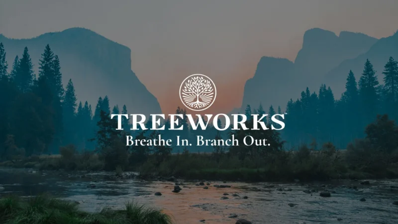 A river flows through a forest with pine trees and mountains in the distance at dusk. The text “TREEWORKS Breathe In. Branch Out.” appears over the scene, with a circular tree logo above the main text.