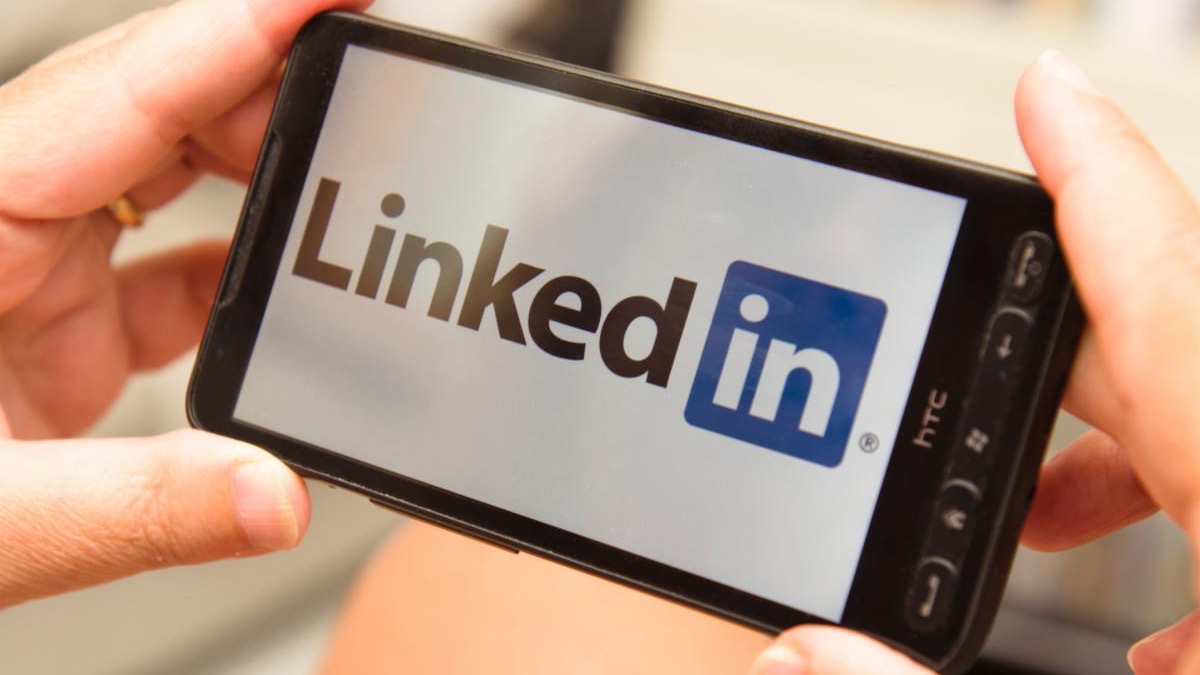 Hands holding a smartphone displaying the LinkedIn logo.