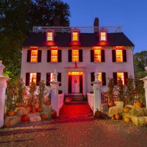 A two-story house with illuminated red windows for CCE Nightlife, decorated with pumpkins, hay bales, and corn stalks lining the entrance walkway.
