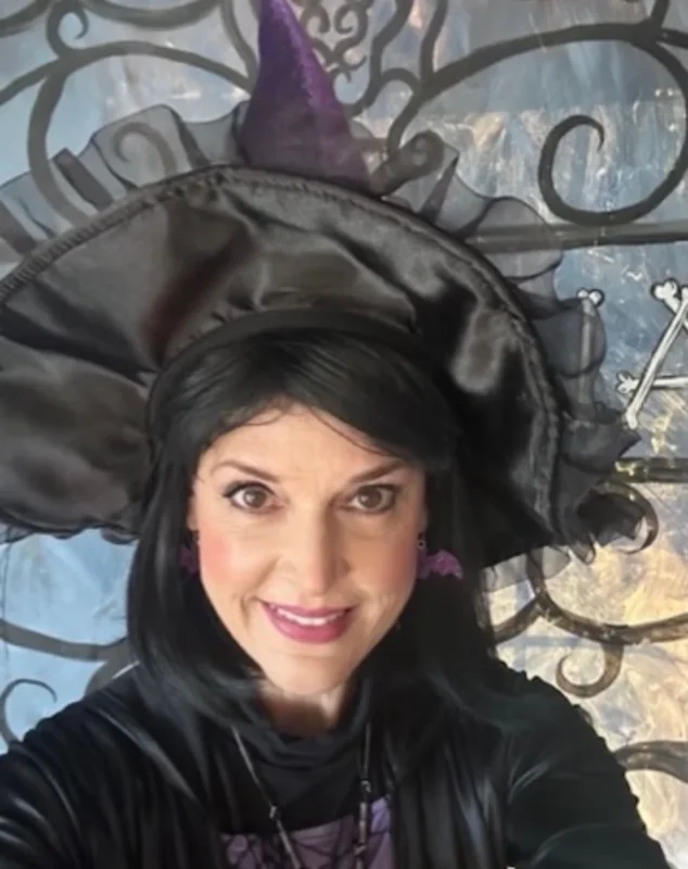 A woman wearing a Halloween witch costume with a black hat and purple accents.