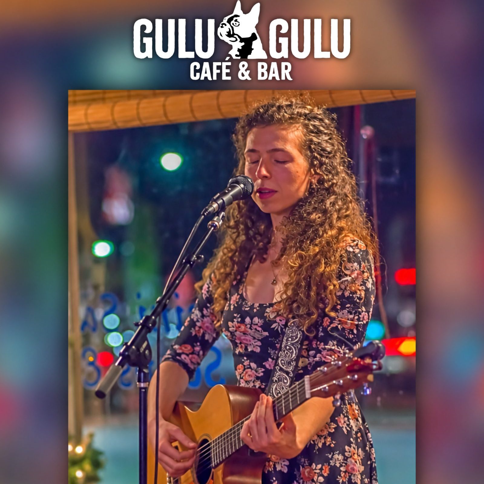 A woman with curly hair plays an acoustic guitar and sings into a microphone at Gulu-Gulu Café & Bar.