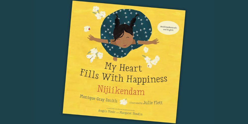Book cover for “My Heart Fills With Happiness / Nijiikendam” by Monique Gray Smith, featuring an illustration of a child lying on a yellow background surrounded by white flowers.