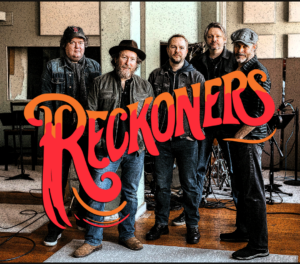 Five men standing in a recording studio with the band name “Reckoners” overlaid in large red and orange stylized text.