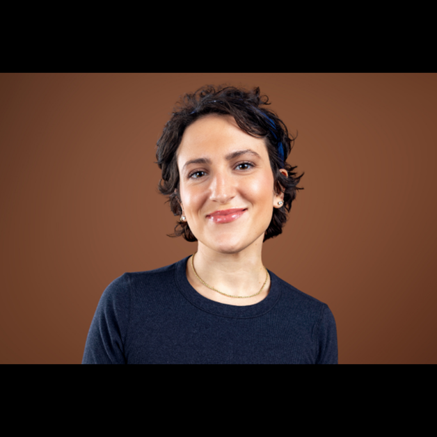 Emily Wilson, a woman with short, curly dark hair, smiles at the camera against a brown background.