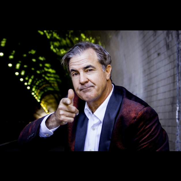 Comedian Jackie Flynn in a tuxedo jacket pointing at the camera inside a tunnel.