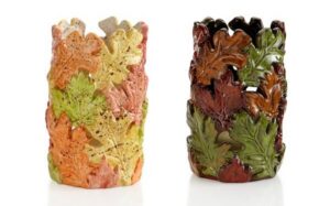 Two cylindrical candle holders shaped like piles of oak leaves, shown in light autumnal colors and dark green tones, perfect for Sevenings in Essex County.