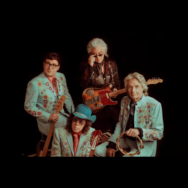Marty Stuart and The Fabulous Superlatives pose in embellished western-style suits, with three of the four musicians holding an electric guitar, a bass guitar, and a tambourine.