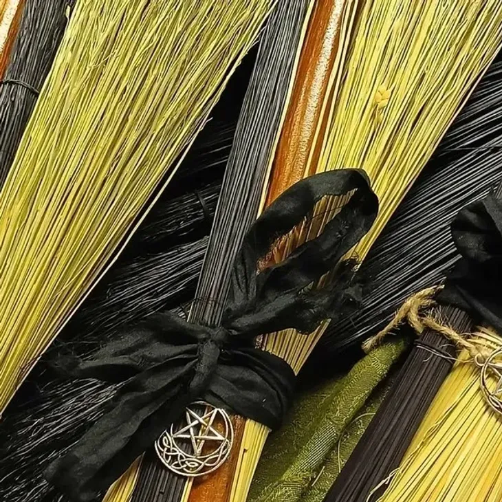 Bundles of black and natural yellow dried broom straw tied with black ribbon and adorned with silver pentacle charms, crafted during a broom making workshop.