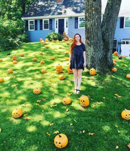 a woman standing next to a tree filled with pumpkins.