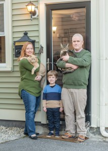 a man, woman, and child standing in front of a door with a cat.
