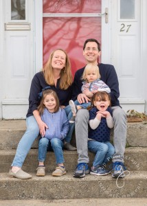 a family sitting on steps in front of a red door.