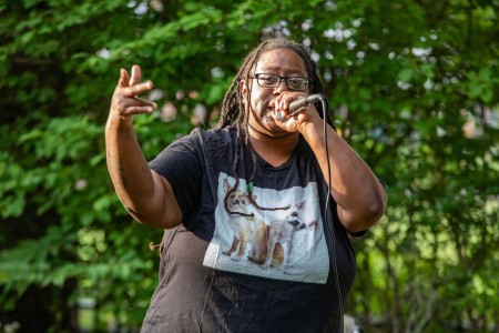 a woman singing into a microphone in front of a tree.