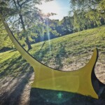 a yellow sculpture in the middle of a park.