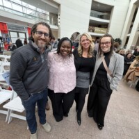 Four smiling people connect at a lively Essex County event, chatting amid white chairs and neighbors, sharing creative energy together.