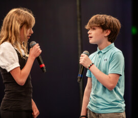 Two young performers sing facing each other on the theatre-in-the-round stage at A Night for Patrick in Beverly, Massachusetts