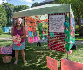 Artist Paula Borsetti laughs beside The Giving Garden, her canopy painted as a brick garden wall and hung with handmade flowers, at the Beverly Garden Party on Beverly Common