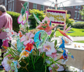 A bouquet of hand-painted fabric flowers in front of the Cornucopia Threads sign at the Beverly Garden Party, with a visitor browsing behind