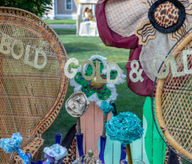 A gold glitter banner reading Bold Gold and Old strung between two peacock wicker chairs at a vintage booth at Beverly's Garden Party